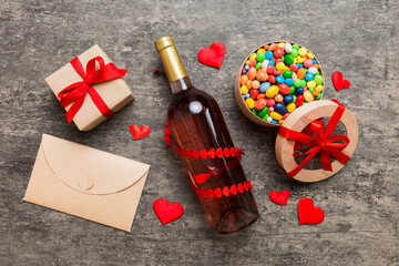 Bottle of red wine on colored background for Valentine Day with gift and chocolate. Heart shaped with gift box of chocolates top view with copy space