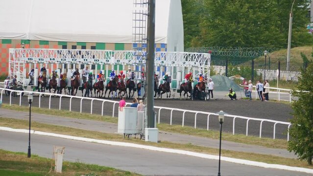Horseback riding sport competition start. Riders on horses begin to gallop at race track at signal. Jockeys in helmets, sportswear on stallions jump out to hippodrome to be first. Equestrian event