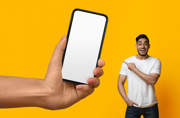 Cheerful arab man pointing at big blank smartphone in giant female hand