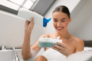 Woman Taking Bath Squeezing Shower Gel On Sponge In Bathroom