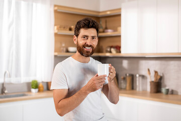 Smiling attractive adult caucasian man in white t-shirt enjoy cup of fresh coffee and spare time