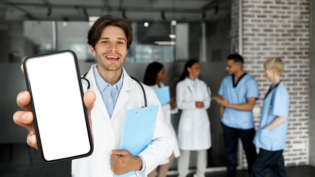 Medical Offer. Smiling Male Doctor Showing Blank Smartphone At Clinic Interior - Powered by Adobe