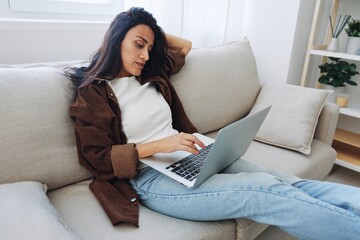 Woman freelancer on day off sitting on sofa with laptop at home online shopping on internet, smile