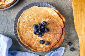pancakes with blueberries on a plate, napkin, wooden spatula on the table, top view