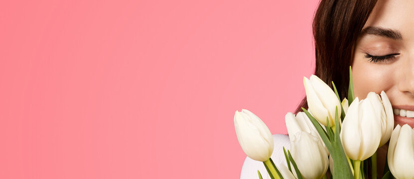 Gift to date, birthday, holiday. Happy young european female with closed eyes smelling white tulips bouquet