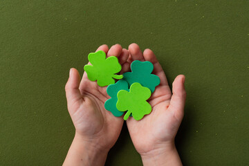 Hands holding a shamrock on green background. A four leaf clover. Good for luck or St. Patrick's day. Shamrock, symbol of fortune, happiness and success. Holding good luck in hands. Close up