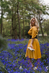 A young woman in yellow dres is walking in a forest with bluebells.Spring is coming.