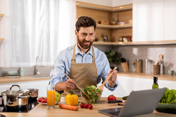 Obraz premium Smiling mature caucasian male in apron preparing dinner, watching video lesson on computer