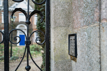 Shallow focus of a metal intercom system seen out a gated entrance to a distant large period house.