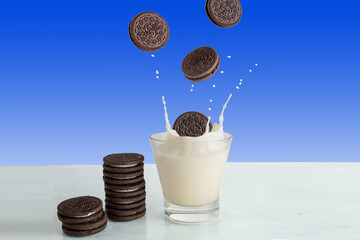 A chocolate chip cookie falls into a glass of milk