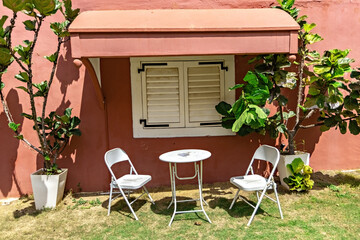 White cafe table and chairs in front of the red wall in the garden