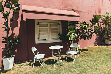 Fototapeta na wymiar White cafe table and chairs in front of the red wall in the garden