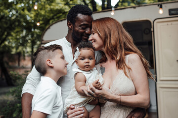 Portrait of candid friendly happy interracial family with two kids outdoor near retro travel trailer