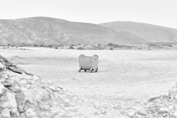 Monochrome: metal trash can on dry land and mountains in the background