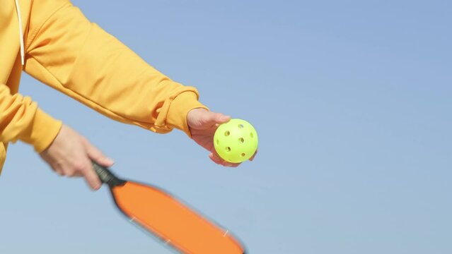 woman playing pickleball game, hitting pickleball yellow ball with paddle, outdoor sport leisure activity