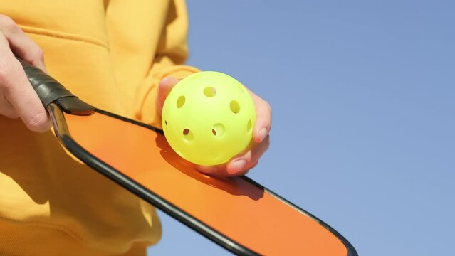 Pickleball paddle and yellow ball close up, woman playing pickleball game, hitting pickleball yellow ball with paddle, outdoor sport leisure activity