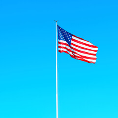 Large national flag of the United States flutters in the wind on a clear sunny day. Bright and vivid pride and unity concept.