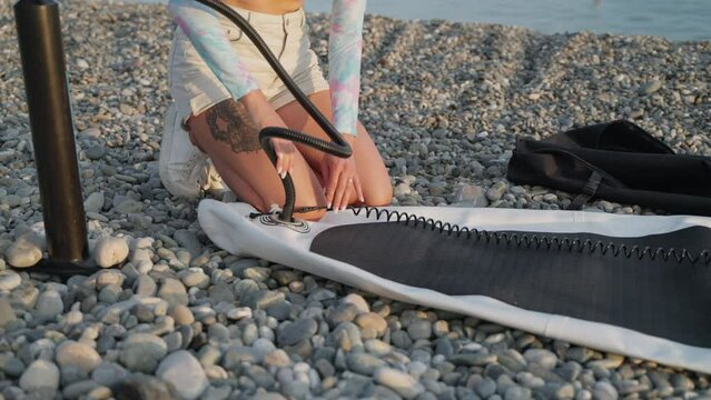 Girl inflating a sup board on the sea coast