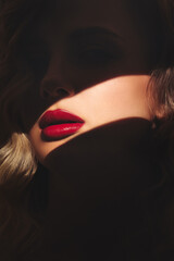 Bright red lips of a blonde woman highlighted by a streak of light.
