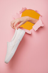 A woman's hand holds a white sneaker through a hole in a pink cardboard.