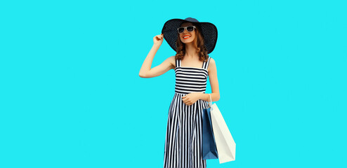 Portrait of happy smiling young woman with shopping bags wearing black round straw hat on blue background