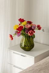 Colorful tulips on the bedside table. Fresh design. Fresh flowers in vase near bed, bedroom interior design details, cozy hotel room, apartment after renovation, modern flat with decor.
