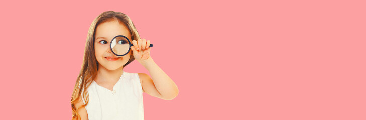 Portrait of child looking through magnifying glass looking away on pink background, blank copy space for advertising text