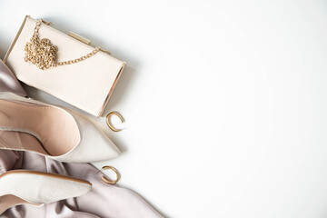 Beige heeled shoes, handbag and earrings are on a white background. Elegant accessories for a wedding or in a restaurant. Copy space.