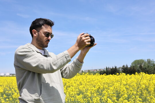 Young man taking photograph with camera in yellow flower field.