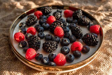 Raspberries and blackberries on a platter with a golden border. Healthy food on a plate.