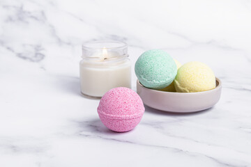 Pink, green and yellow bath bombs and candle on marble background. Bath salts