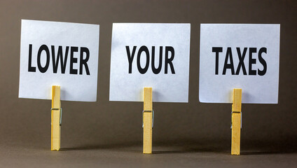 Lower your taxes symbol. Concept words Lower your taxes on white paper on clothespin on a beautiful grey table grey background. Business tax lower your taxes concept. Copy space.