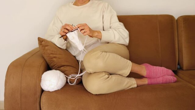 Woman sitting at home on sofa with her feet in wool socks and knitting