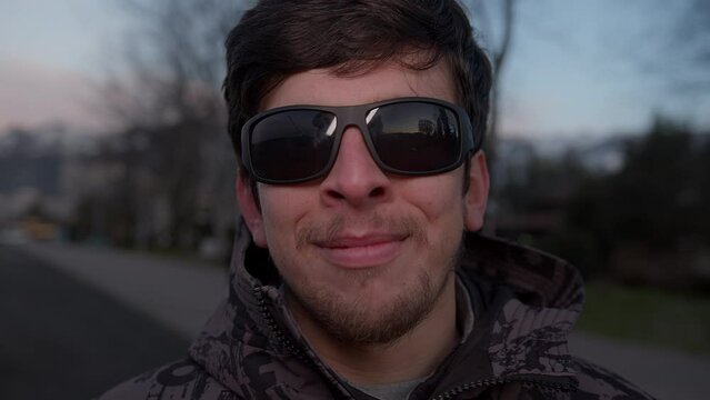 A Handsome Young Man in Sunglasses Smiling at the Camera Outdoors in a Stylish Coat