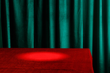 Background with empty red cloth table and green draped velvet curtains. Template for advertising,...