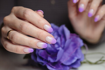Female hands with violet nail design close-up. Artistic manicure with gradient violet glitter nail polish