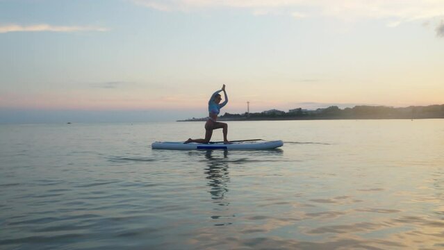 Girl practicing yoga on paddleboard at sunset
