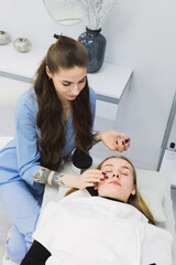 A patient with bad facial skin lying on a treatment table while a cosmetic dermatologist performs a procedure on her.