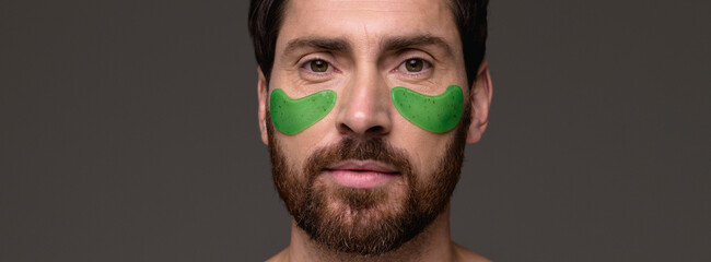 Banner view of bearded man with hydrogel patches on face isolated on grey background 