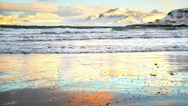 Beach with White Mountains with snow are washed by the cold sea. Beautiful winter nature background landscape at sunrise in Iceland. Shot in 8k Resolution 4320p