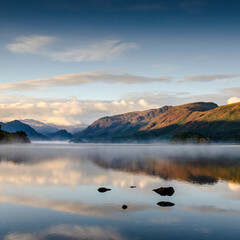 Fells reflected in a still and misty lake at dawn
