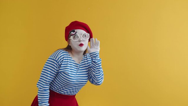  A young mime girl in bright clothes puts her hand to her ear pretends to eavesdrop on gossip and covers her mouth with her hand in surprise