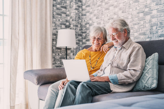 Pretty Elderly 70s Grey-haired Couple Resting On Couch In Living Room Hold On Lap Laptop Watching Movie Smiling Enjoy Free Time, Older Generation And Modern Wireless Technology Advanced Users Concept.