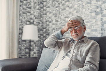Fototapeta premium Frustrated unhealthy senior mature man touching head, having painful feelings sitting alone at home. Unhappy middle aged retired grandfather suffering from high blood pressure disease indoors..