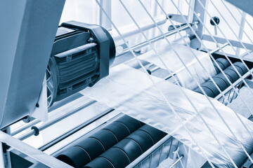 Fototapeta premium Automatic polyethylene plastic bag production machine with lighting effect. Close-up of the roller of the plastic bag production machine in the light blue scene. product packaging concept