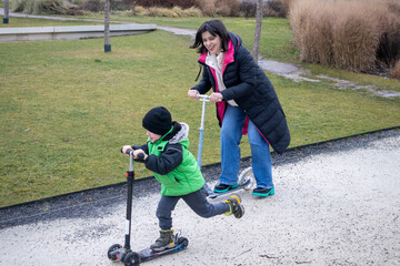 Fototapeta premium A mother and her son learn to ride a scooter in the park