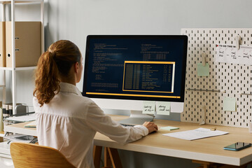 Back view female programmer writing code working at desk