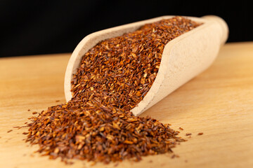 Rooibos tea medium cut in wooden scoop on wooden board. Rooibos in latin Aspalathus linearis. herb....