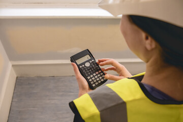 Unrecognizable female civil engineer calculating with a calculator in a construction site, wears...