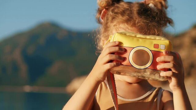 Smiling girl makes photos with a toy camera on a beach